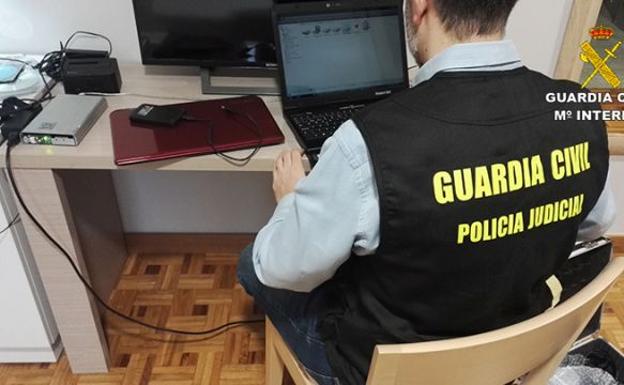Un agente de la Guardia Civil analiza uno de los ordenadores incautados. /